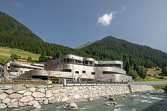 The Silvretta Therme in Ischgl behind a river in the valley in front of the mountains.